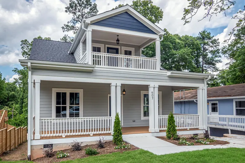 A white two-story house with a deep front porch on a tree-lined street