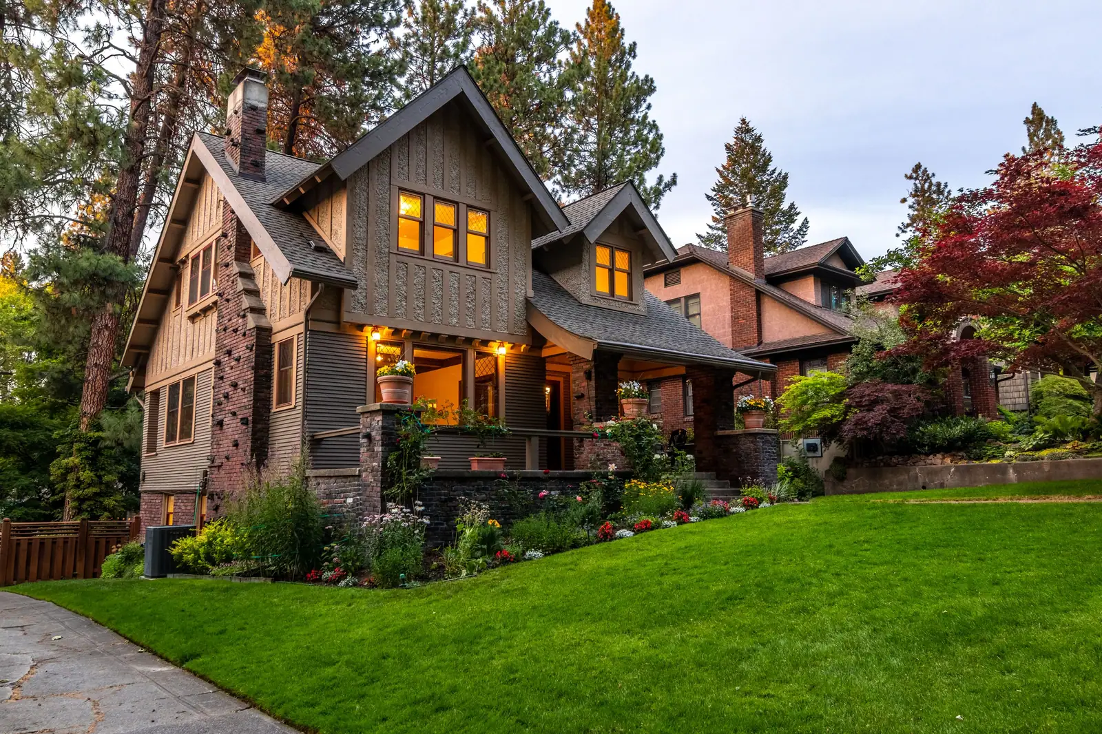The Craftsman house at dusk, its windows lit, with the garden path leading to the front porch