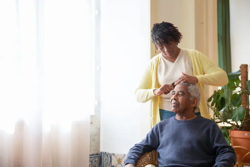 A caregiver combing a resident's hair by the sunny front window