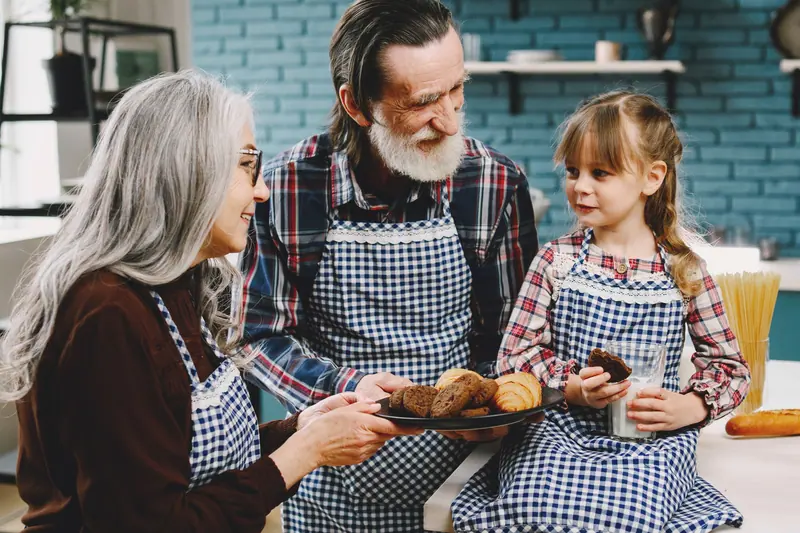 Grandparents in aprons sharing cookies with a granddaughter
