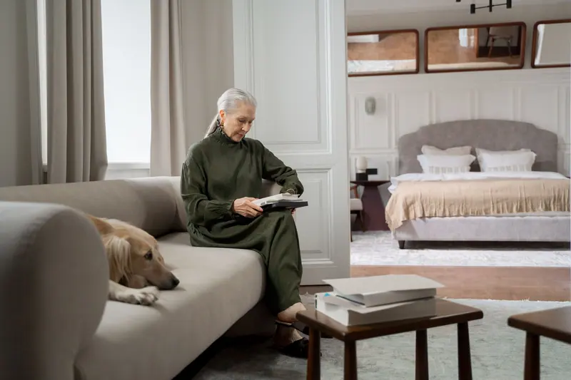 A resident reading on her sofa with her golden retriever beside her