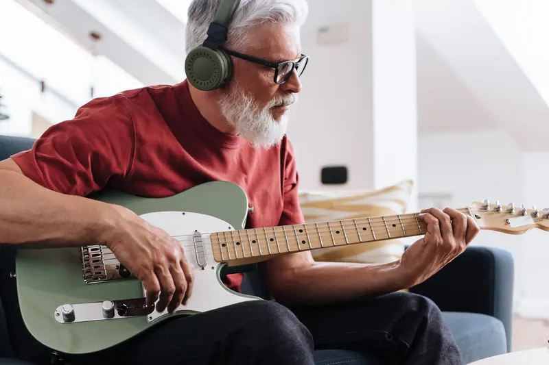 A resident playing electric guitar with headphones in his loft