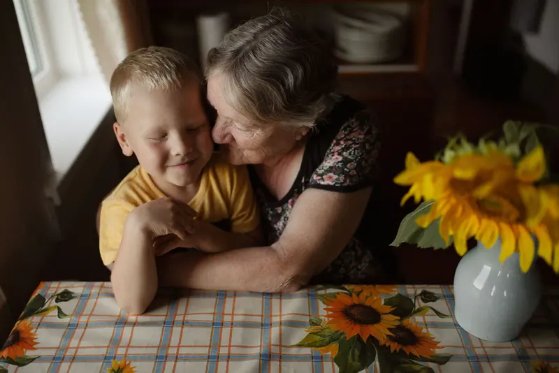 A resident holding her grandson close at a kitchen table set with sunflowers