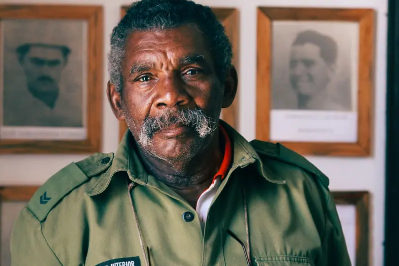 A resident in his old uniform shirt in front of framed photographs from his service