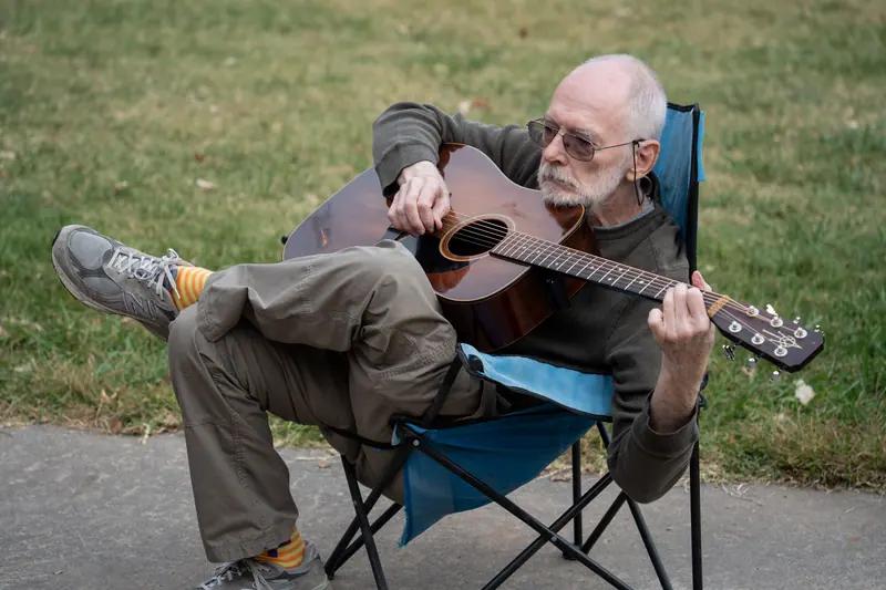A resident playing guitar in a camp chair on the lawn