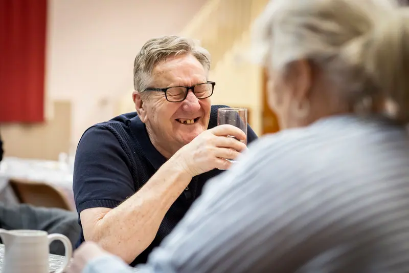 A resident laughing over coffee with a friend in the dining room