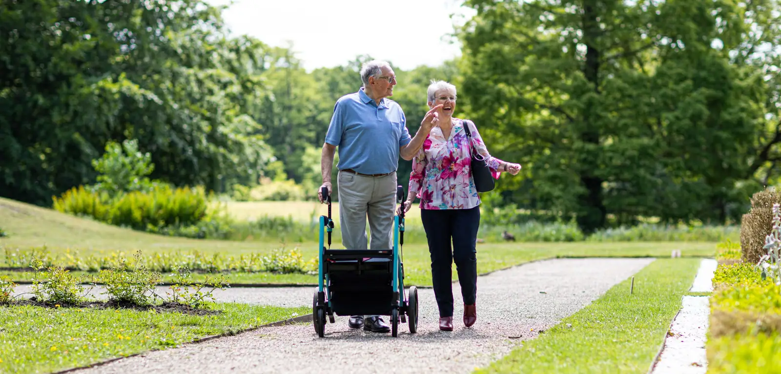 A couple strolling the garden path together, he with his walker and she arm in arm
