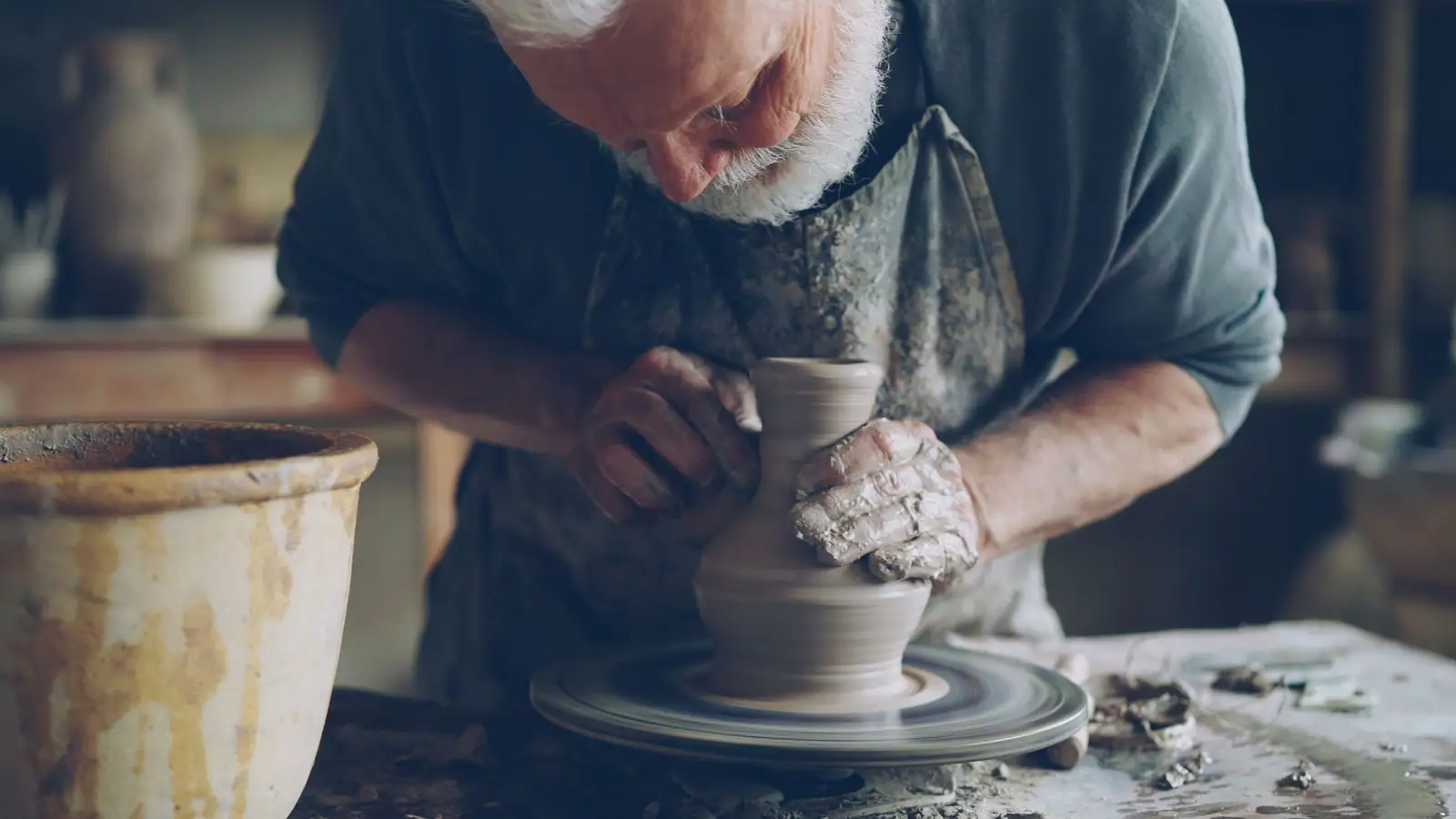 Shaping clay at the wheel, hands covered in slip
