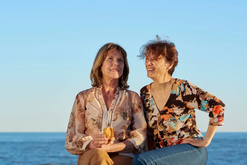 Two longtime friends laughing together by the water on a bright afternoon