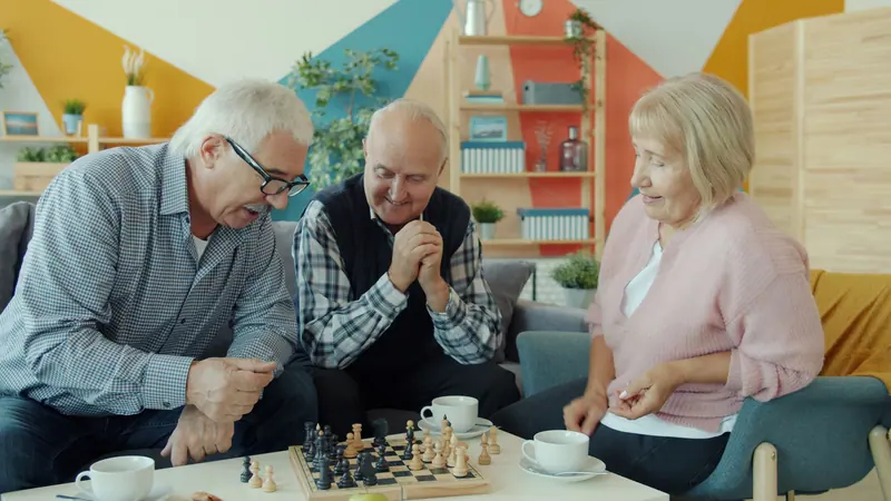 Three friends leaning over a chess game in the sitting room