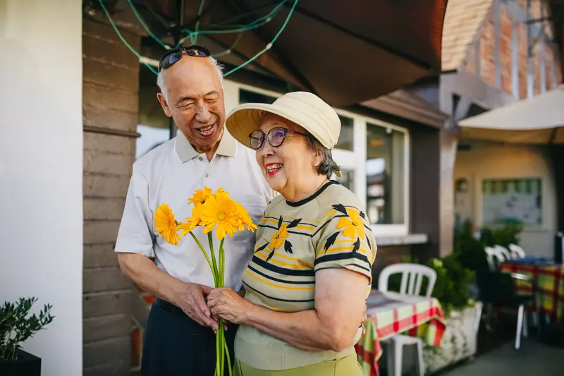 A husband surprising his wife with yellow flowers on the front walk