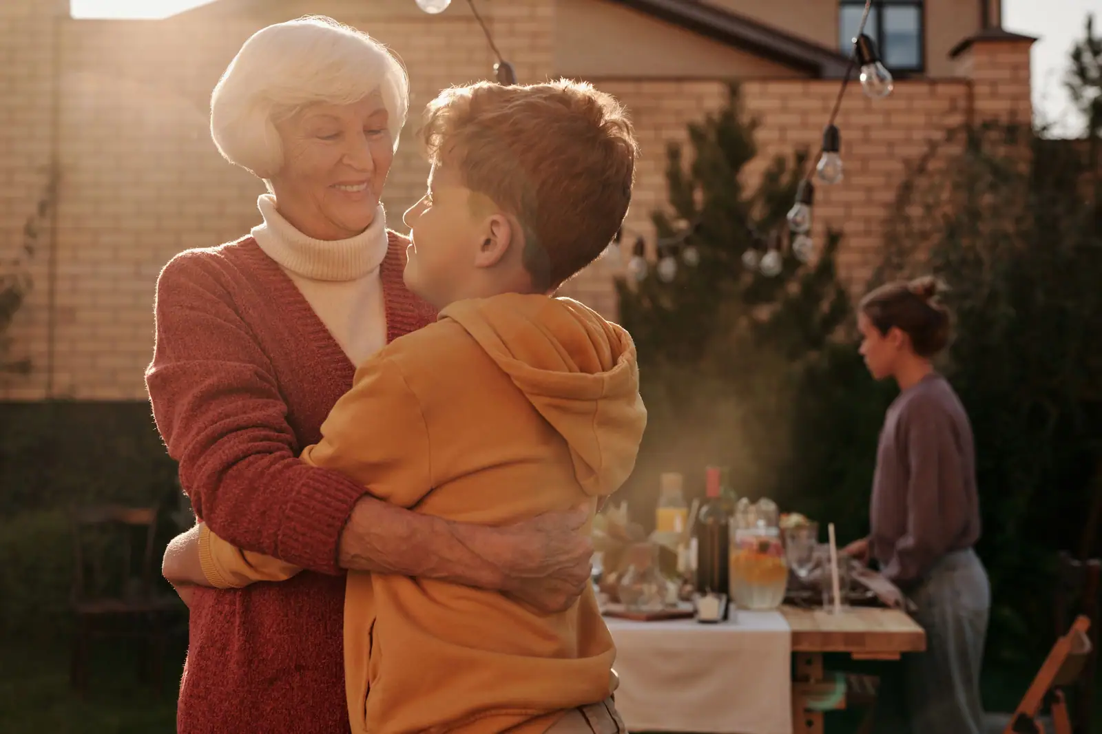 A grandmother hugging her grandson at a golden-hour supper in the courtyard