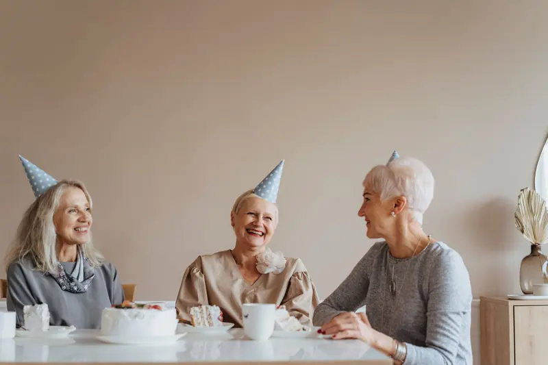 Three residents at a birthday tea, wearing paper party hats