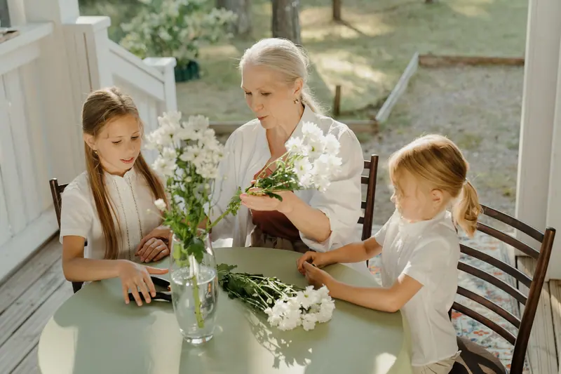 A resident arranging white flowers with her granddaughters on the porch
