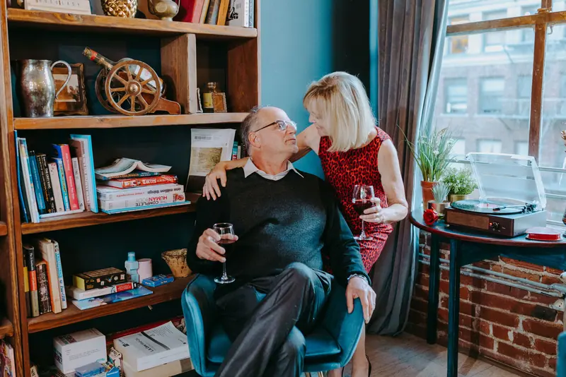 A couple sharing a glass of wine in their cottage sitting room, surrounded by books