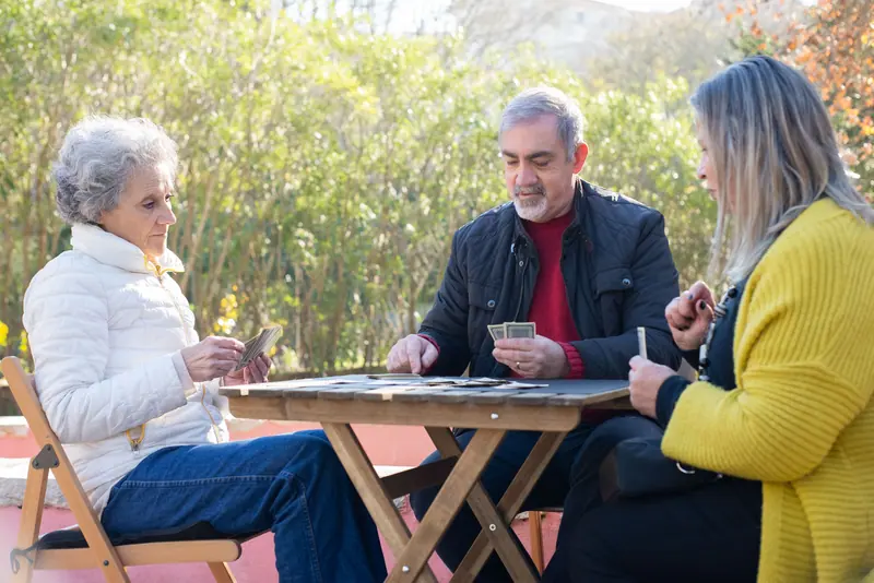 Three neighbors playing cards at a wooden table outside
