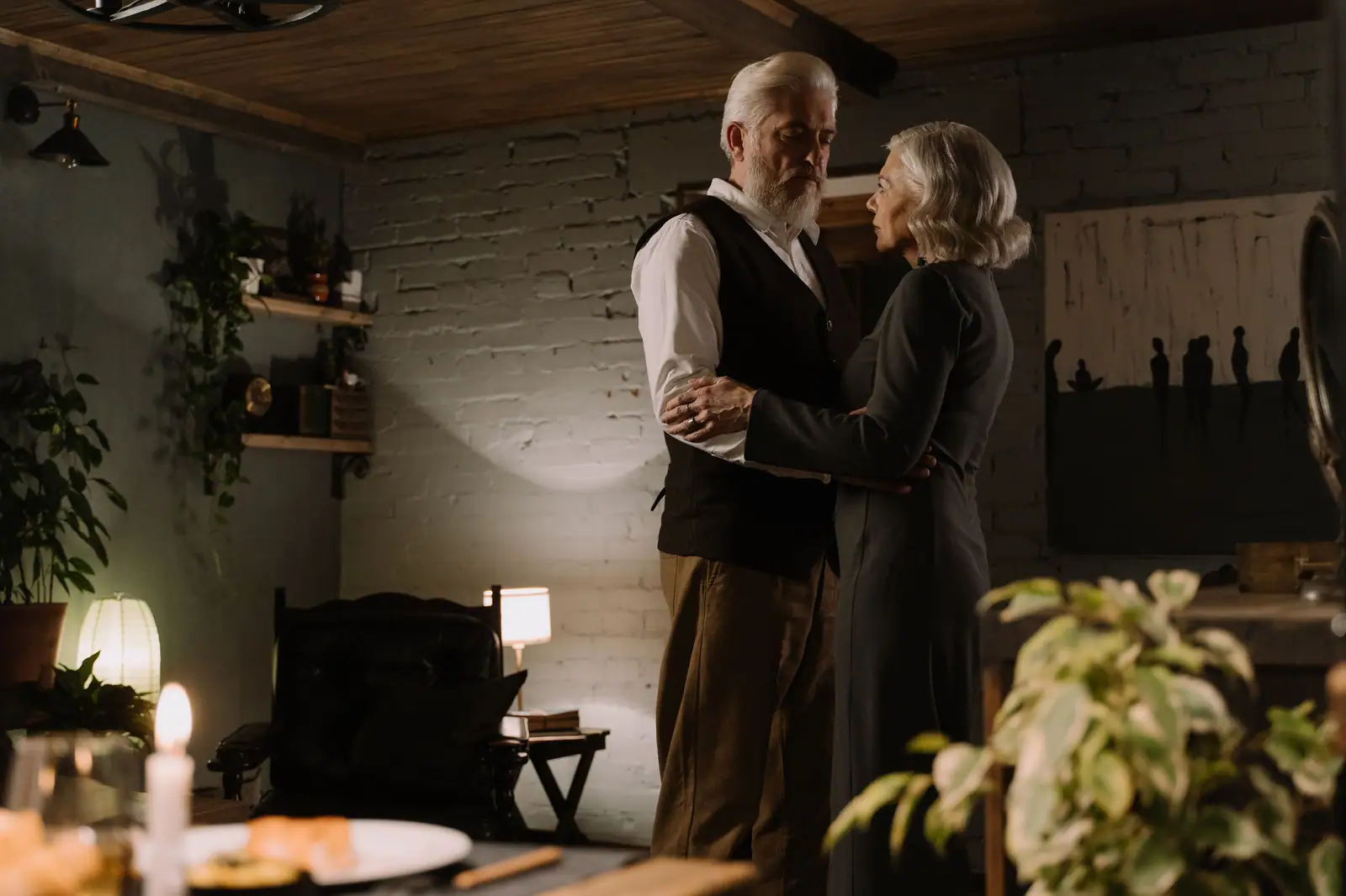 An older couple dancing close in a softly lit room with a candle burning nearby