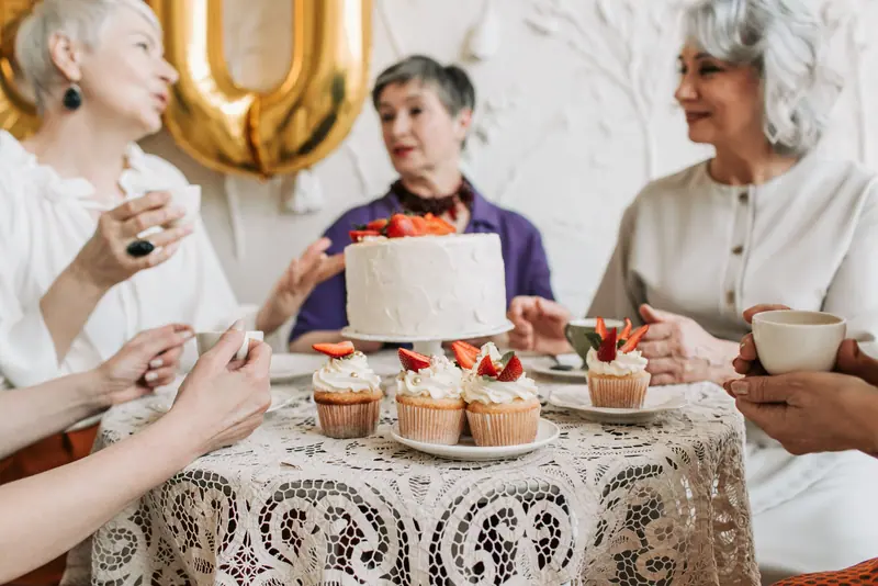 Friends gathered around a lace tablecloth and a strawberry cake