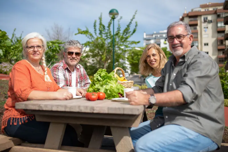 Residents and a daughter around a picnic table piled with vegetables from the garden