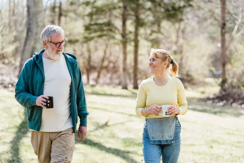 Two neighbors carrying coffee mugs across the back pasture on a spring morning
