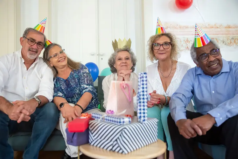 Residents in party hats gathered on the sofa with a stack of birthday presents