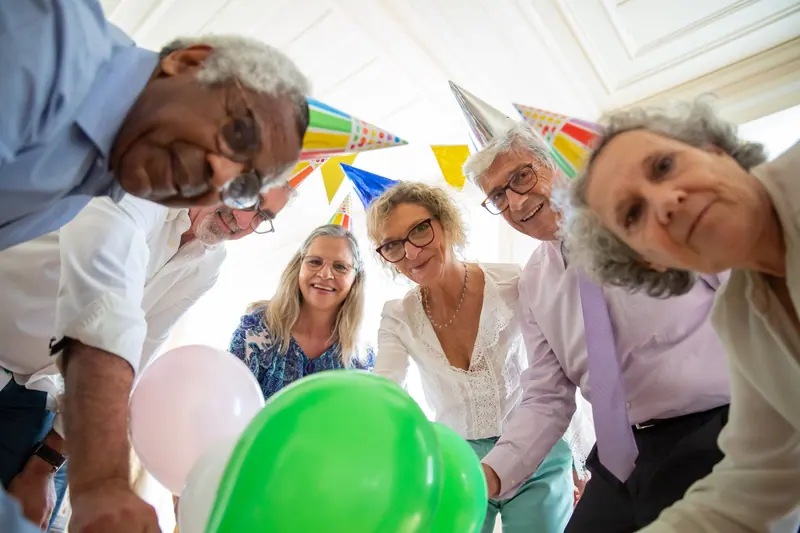 Party guests leaning in for a group photo with green balloons