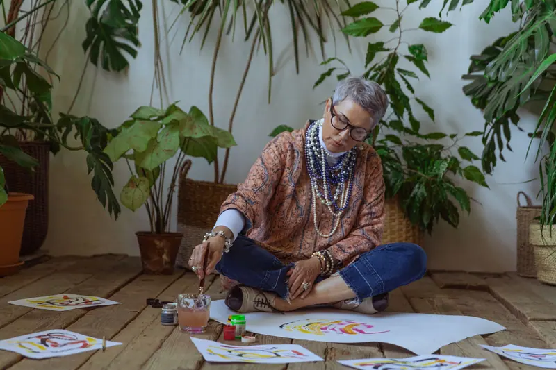 A resident working on watercolors on the studio floor among potted plants