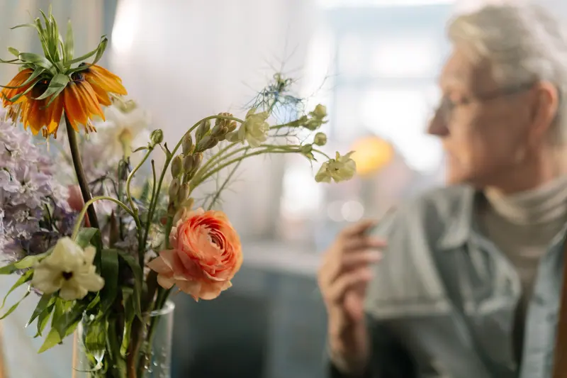 A resident admiring a vase of ranunculus by the window