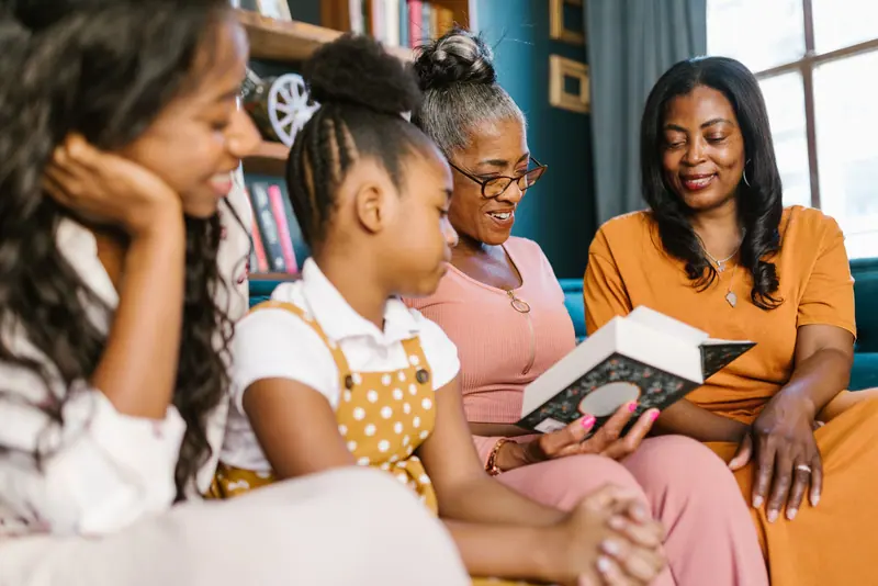 Three generations reading together on the sofa during a family visit