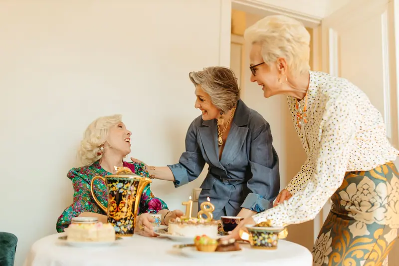 Friends sharing cake and laughter at a small birthday tea in the parlor
