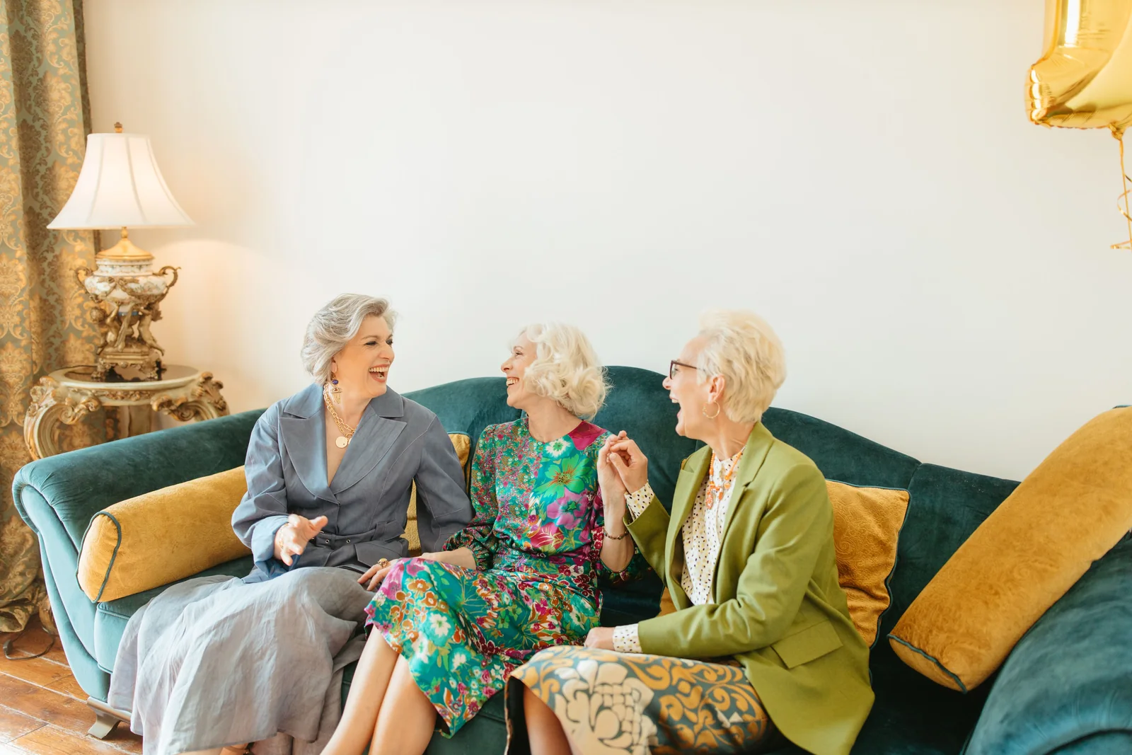 Three friends laughing together on a teal sofa