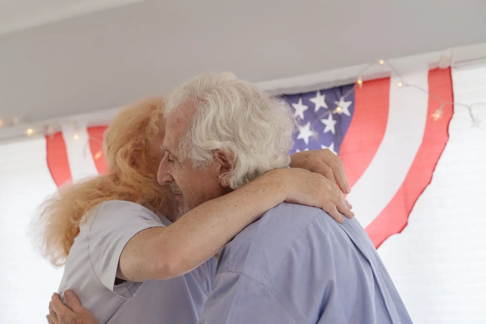 A resident and his wife embracing in front of the American flag at the Veterans Day reception
