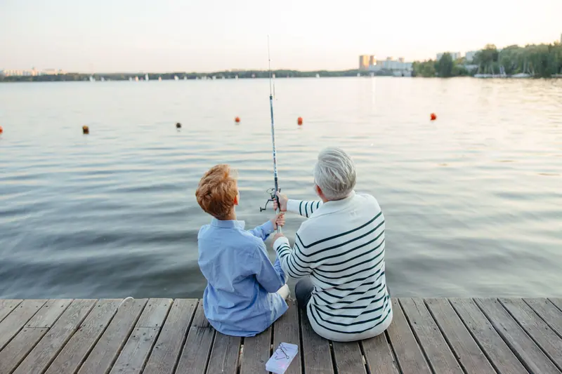 A grandfather teaching his granddaughter to fish at sunset