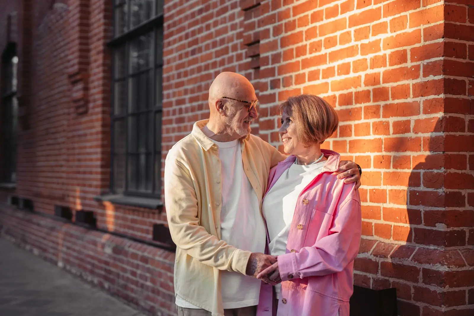 An older couple laughing together against a sunlit brick wall
