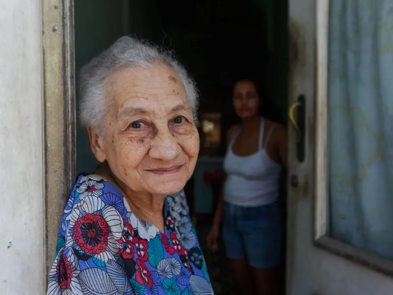 A smiling resident in a flowered dress at the door of her room