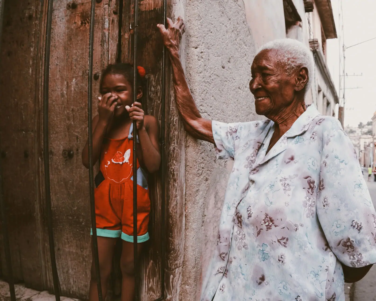 A resident laughing in her doorway as her great-granddaughter peeks around the frame