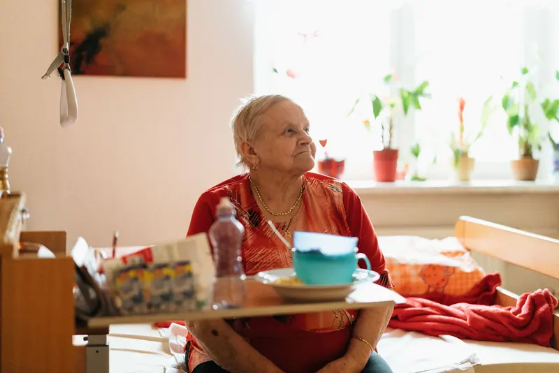 A resident sitting at the table in her room with her tea and flowers