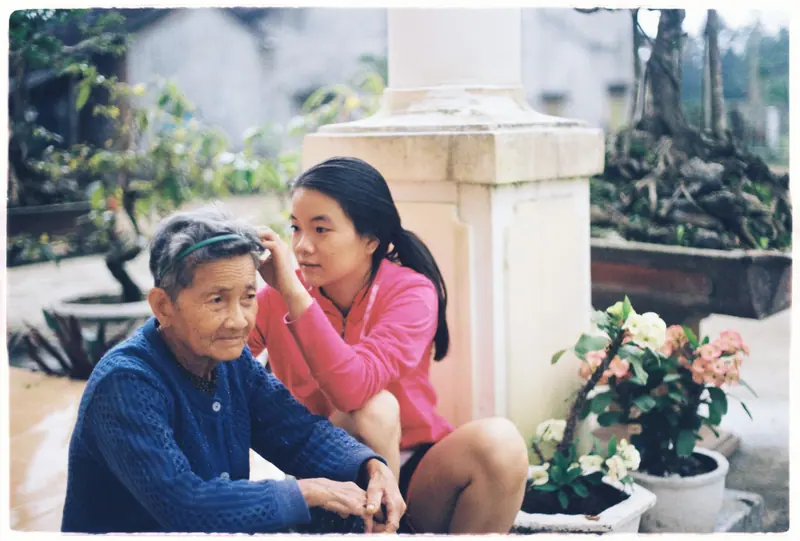 A granddaughter tucking a flower behind her grandmother's ear in the courtyard