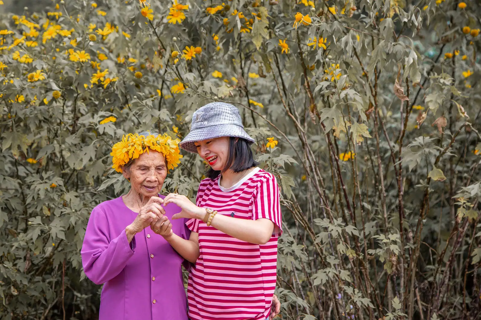 Elderly woman and young woman bonding in a garden full of blooming flowers.