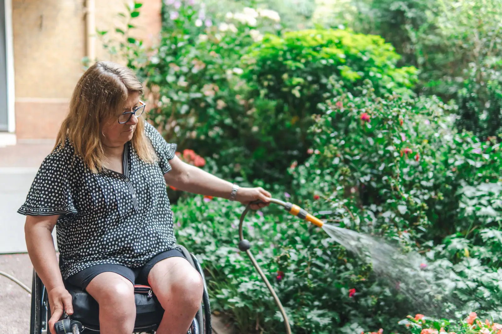 A resident in her wheelchair watering the flower beds in the courtyard garden