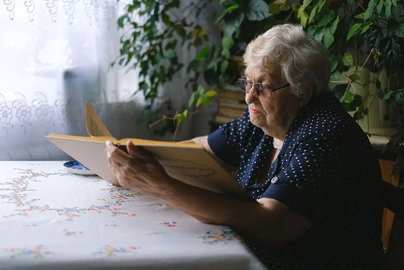 A resident reading her mail at a lace-covered table by the window