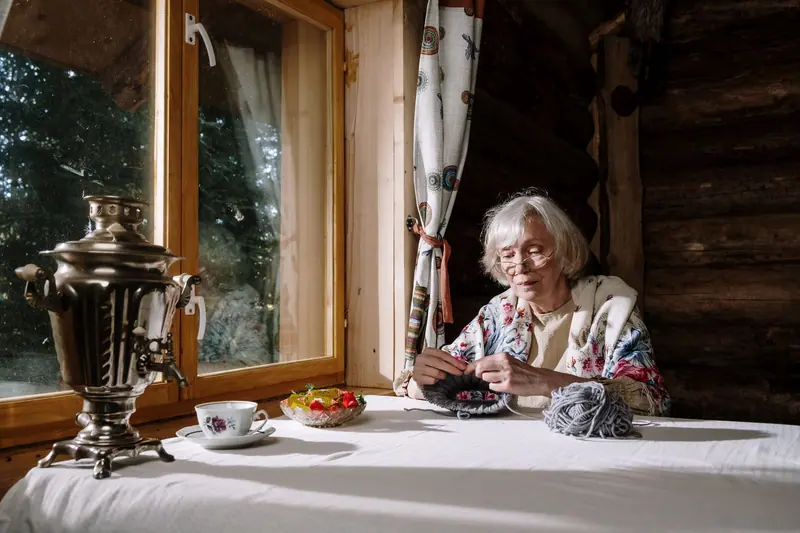A resident knitting at a table by the window with a cup of tea beside her