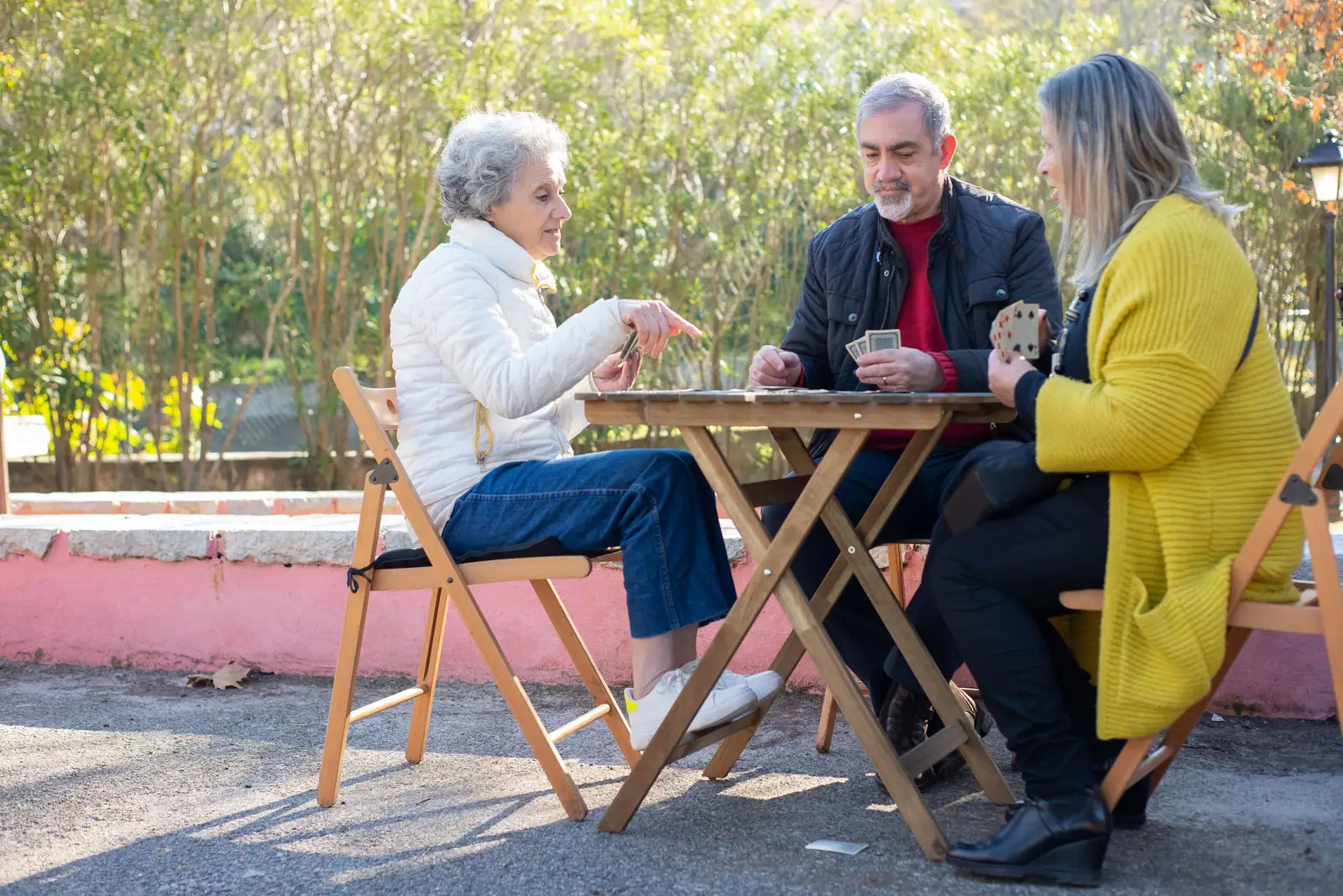 Residents and an aide laughing over a card game at a sunny patio table