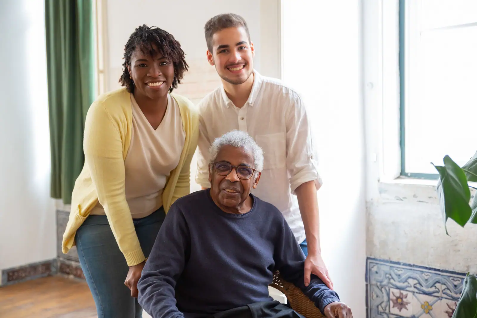 Two caregivers smiling with a resident in his chair