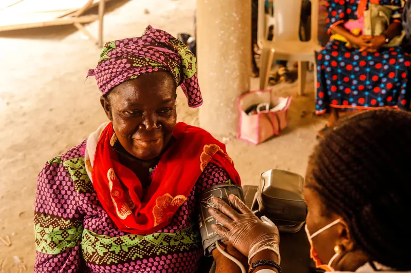 A resident in a bright head wrap smiling during a blood-pressure check