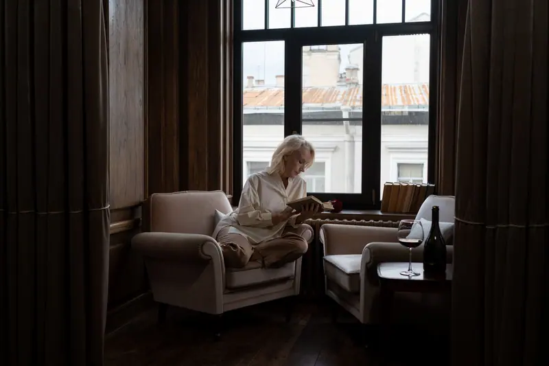A resident with a glass of wine and a novel in the parlor